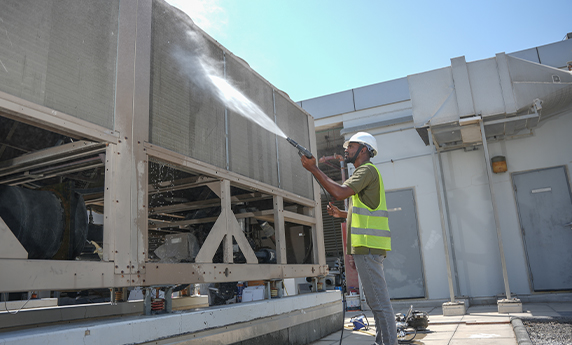 a man wearing a safety vest spraying water on chiller in roof of building